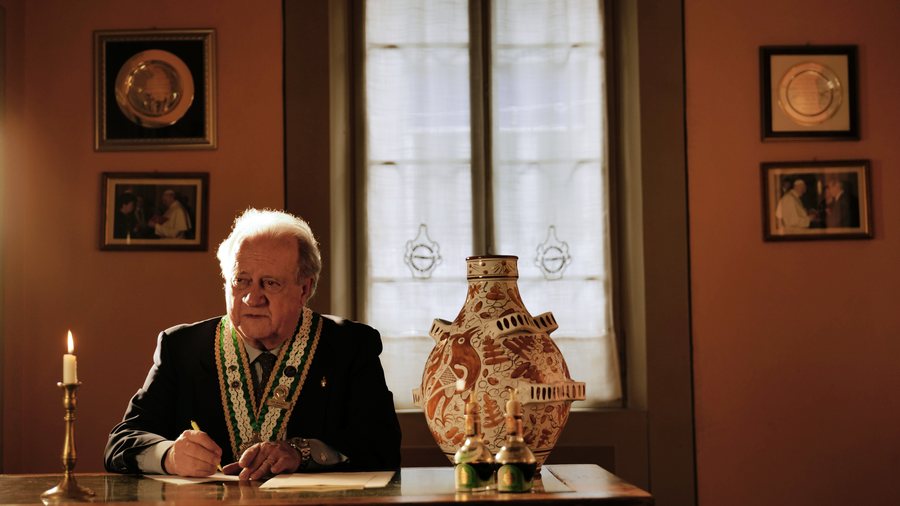 Il Gran Maestro scrive al tavolo, accanto al tragno dipinto